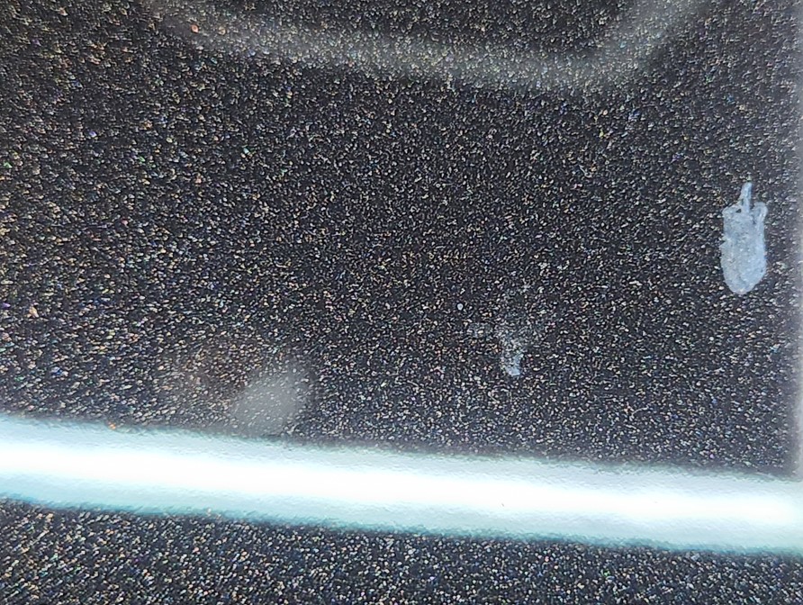 Close-up of fine bonded contamination remaining on black paint after a maintenance wash, showing the limit of normal washing