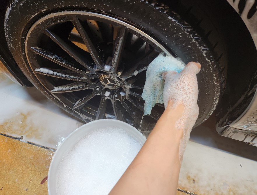 Cleaning a black alloy wheel with a microfiber towel reassigned from paint use and kept separate from body-wash tools