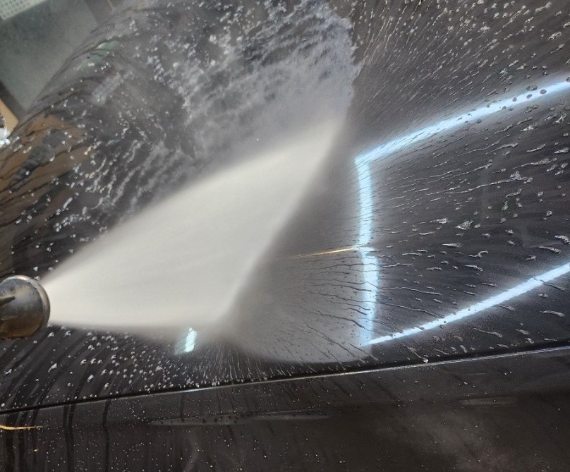 High-pressure water striking automotive paint to remove loosened dirt and cleaning solution