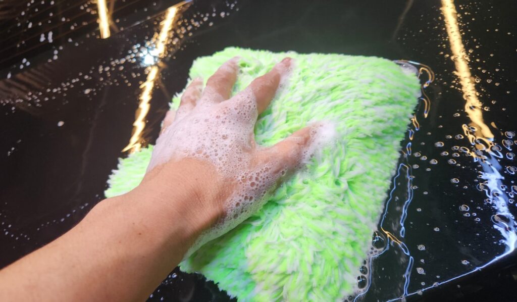 Long-pile microfiber wash mitt cleaning automotive paint with lubricating shampoo solution