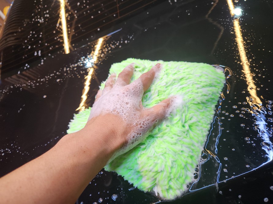 A saturated microfiber wash mitt releasing shampoo solution in the direction of travel to lubricate the paint and flush away loosened contamination