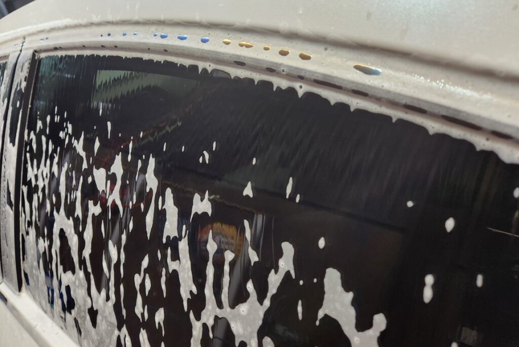 Acid pre-wash foam beginning to dry along a vehicle window trim and panel gap