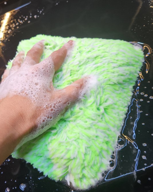 Long-pile microfiber wash mitt carrying shampoo solution across vehicle paint